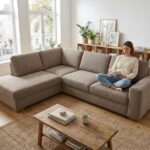 Femme lisant sur un canapé d'angle taupe dans un salon scandinave lumineux et bien aménagé