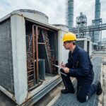 Ingénieur inspectant un condenseur industriel sur le toit d'une usine avec clipbard et équipements de protection