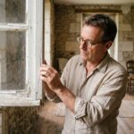 Homme inspectant le cadre abîmé d'une vieille fenêtre en bois dans une maison ancienne en pierre